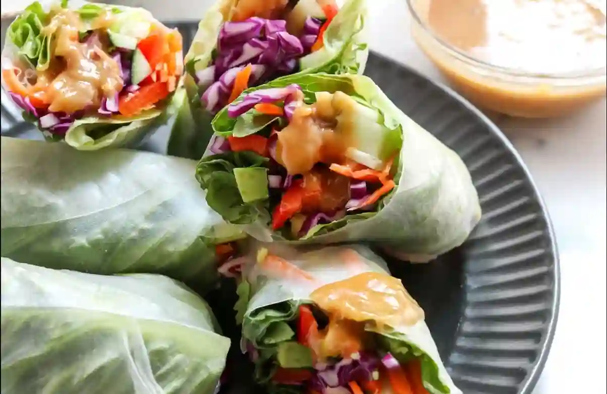 Fresh hearty veggie rolls with peanut sauce on a wooden board.